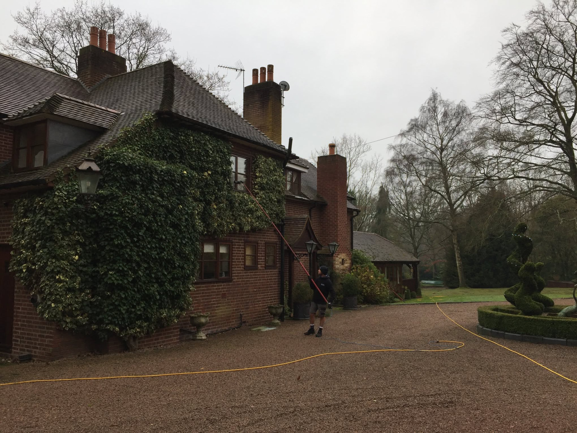 Window cleaner using a water-fed pole on a large ivy-clad country house