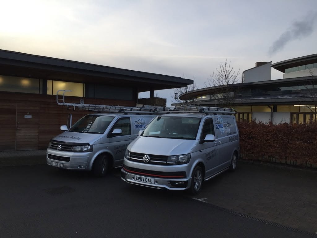 Two Your Home Window Cleaning vans parked outside a modern commercial building