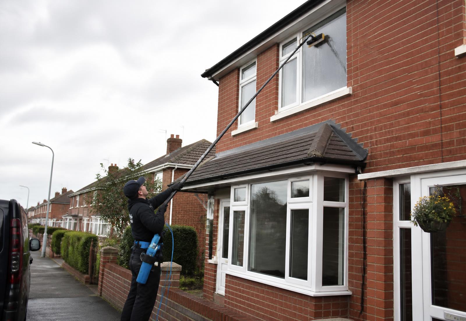 Window cleaner using a water-fed pole on an upstairs window of a brick house